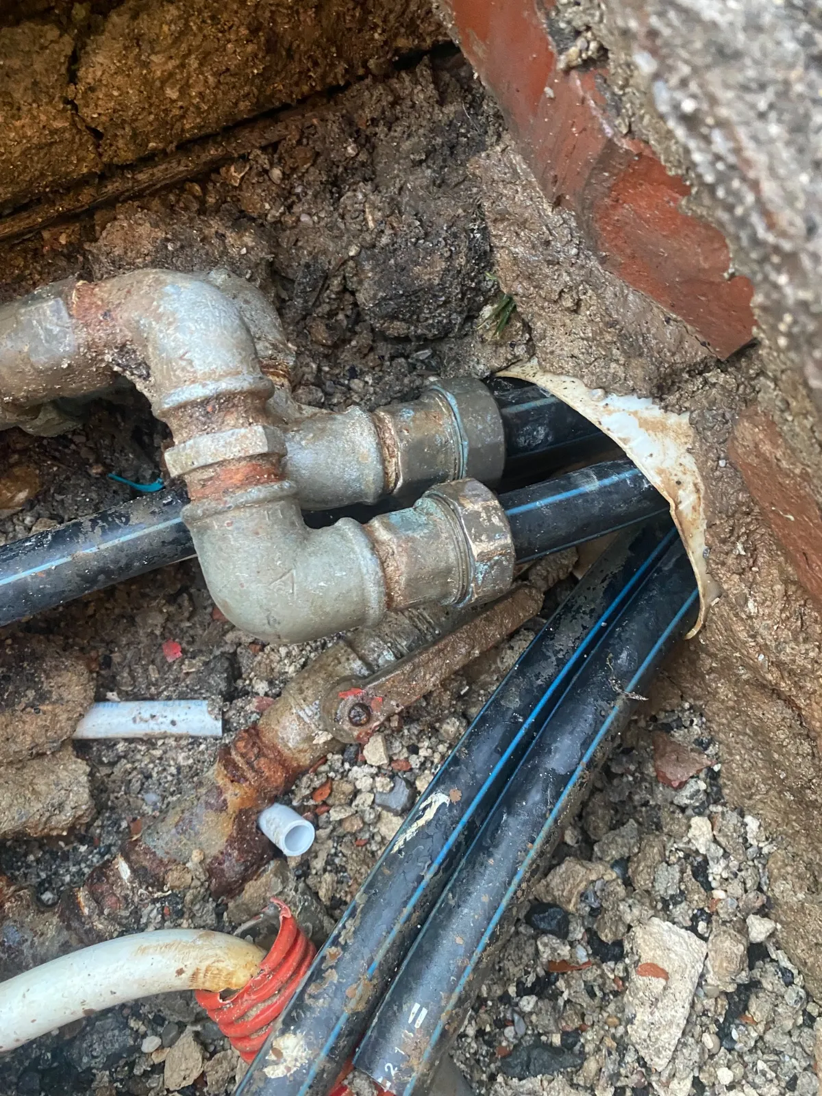 Gli stessi raccordi metallici e i tubi neri a righe blu nello scavo accanto al muro in mattoni, ora senza getti d'acqua