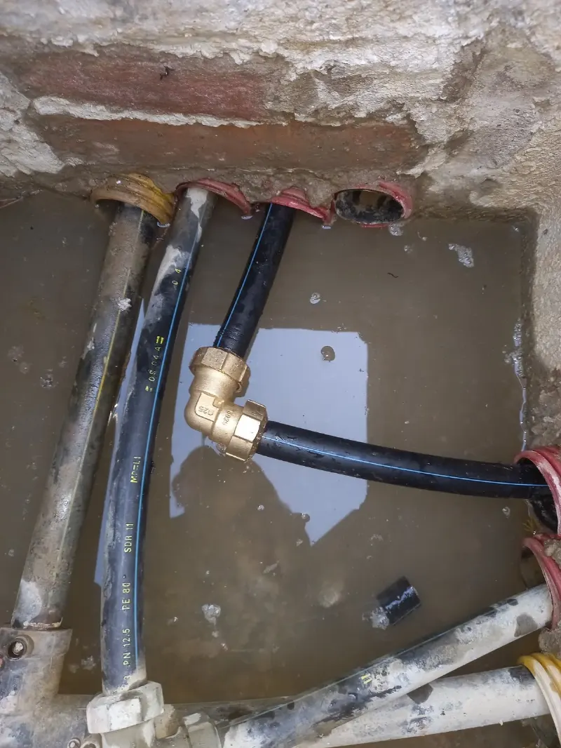 Pozzetto con acqua sul fondo: tubo in polietilene nero a riga blu collegato con un gomito in ottone vicino alle guaine corrugate rosse