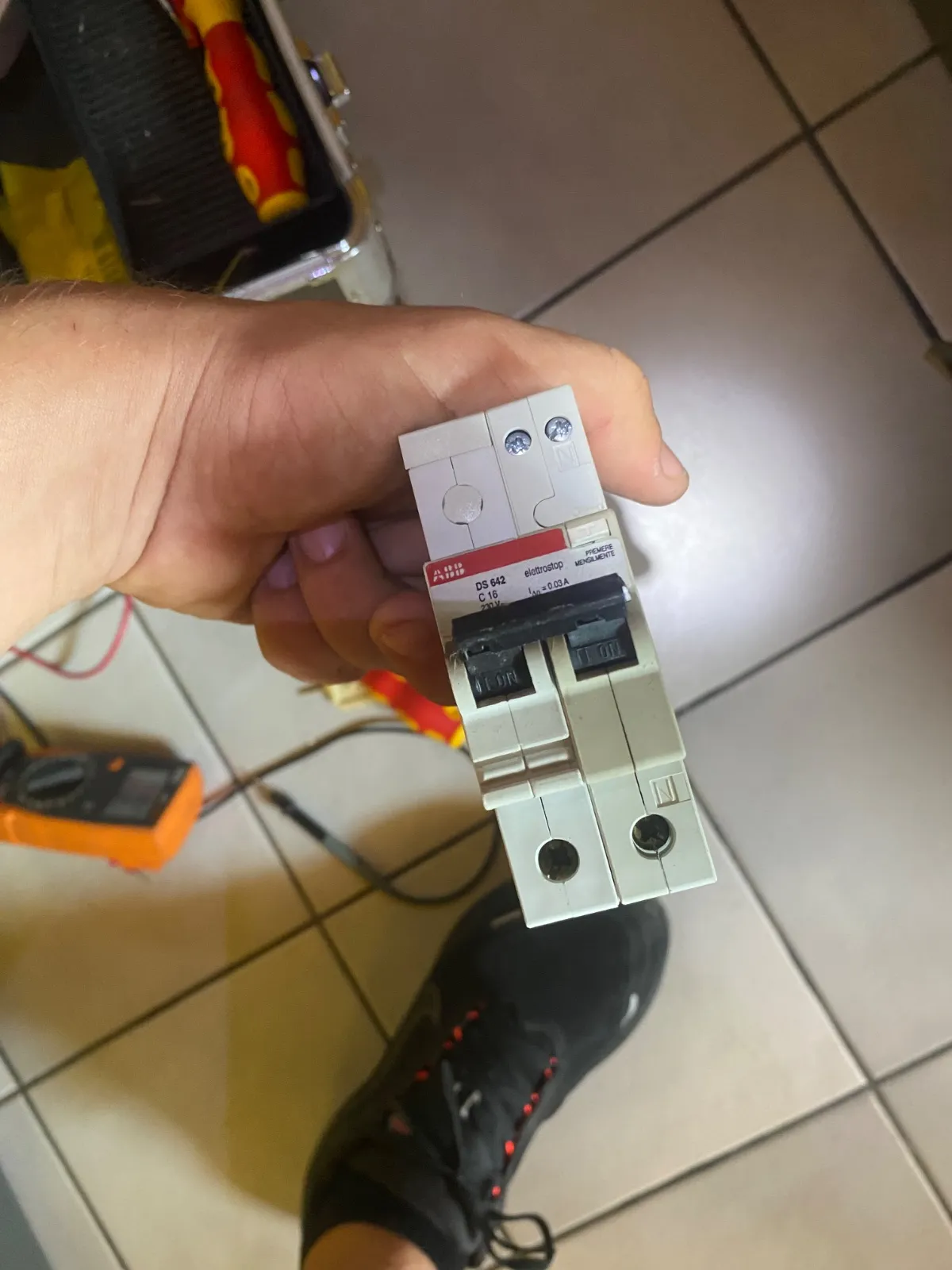 Salvavita a due moduli tenuto in mano fuori dal quadro, con tester e cacciaviti isolati sul pavimento