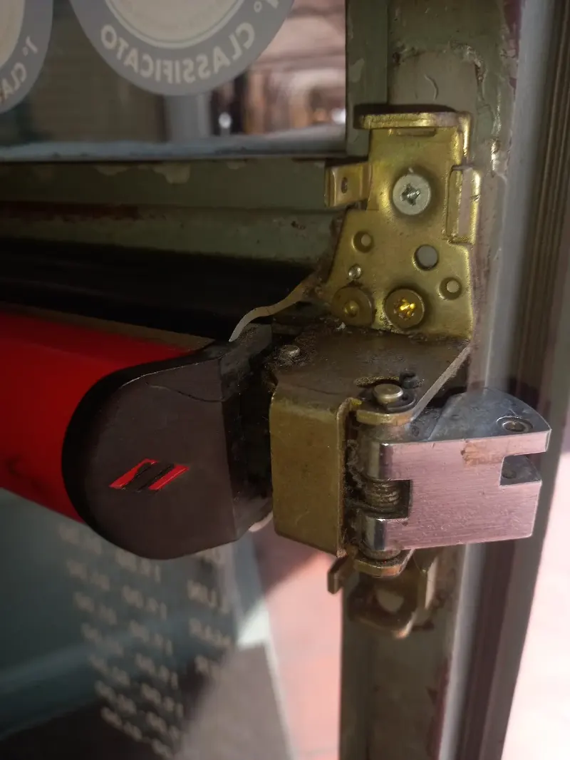 Testata di un maniglione antipanico rosso e meccanismo di chiusura in metallo avvitato sul montante di una porta a vetri