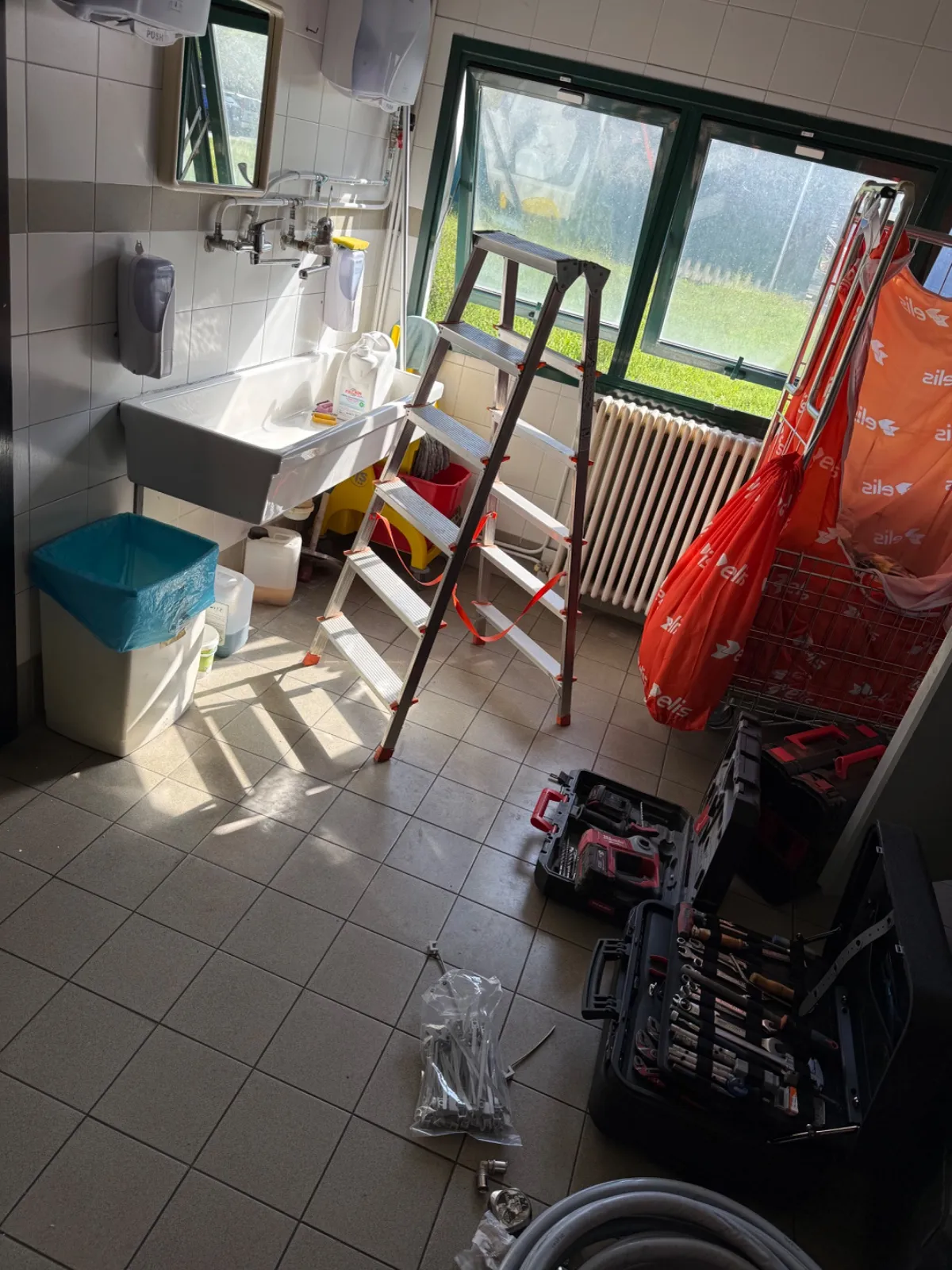 Bagno di servizio con lavatoio e tubi a vista, scala, cassette degli attrezzi e un rotolo di tubo a terra durante i lavori