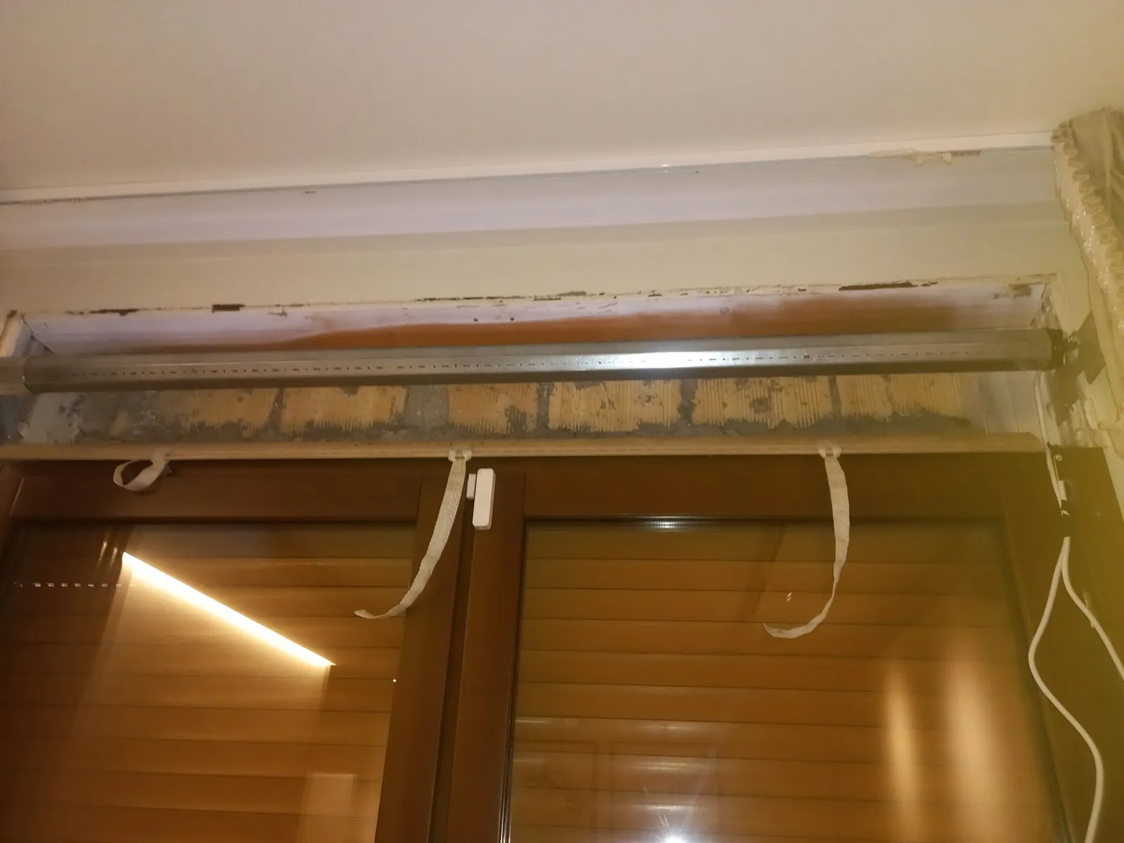 Cassonetto aperto sopra la finestra: il rullo ottagonale in vista e gli attacchi dell'avvolgibile staccati che pendono